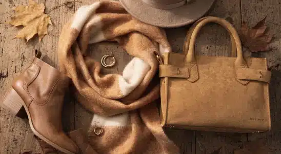 Collection of chic fall accessories including a scarf, leather handbag, and wool hat on a wooden background