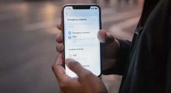 A person holding a smartphone on a city sidewalk at dusk with emergency settings on screen